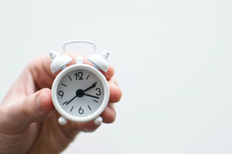Person holding a small alarm clock to represent the guide to time blocking