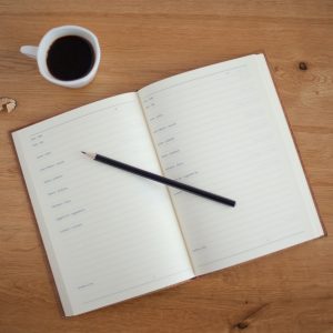 Notebook on a table, with a pencil and cup of coffee to prepare the weekly review